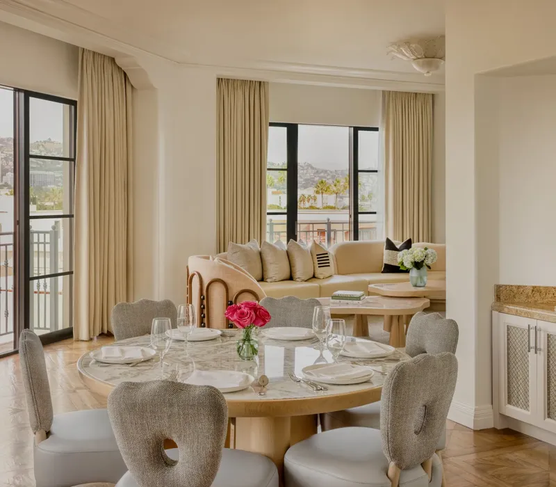 Hollywood Suite dining area with round table, cushioned chairs, with a curved couch in the foreground with Beverly Hills skyline views.