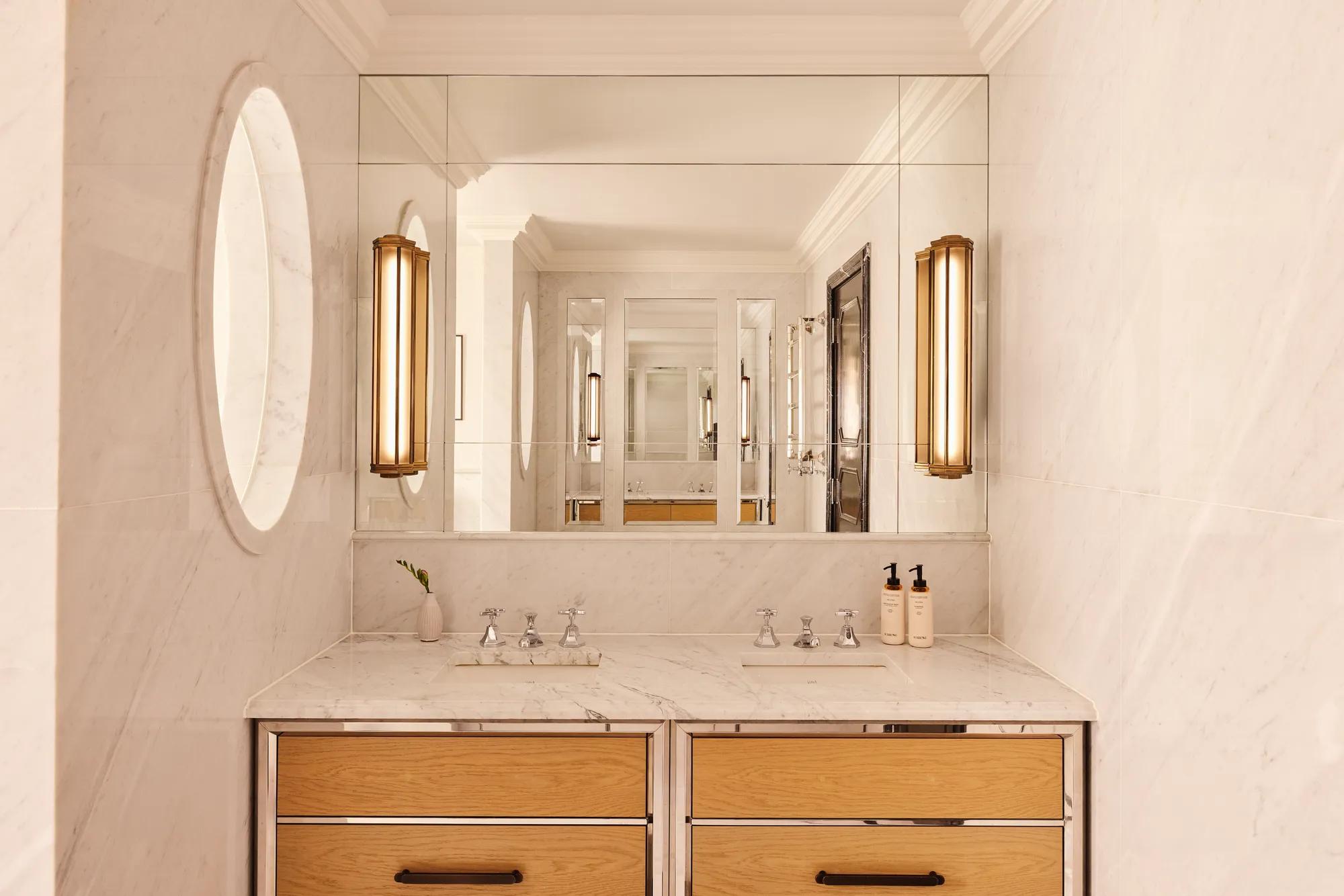 Marble bathroom vanity with double sinks, large mirror, wooden drawers, and wall lights.