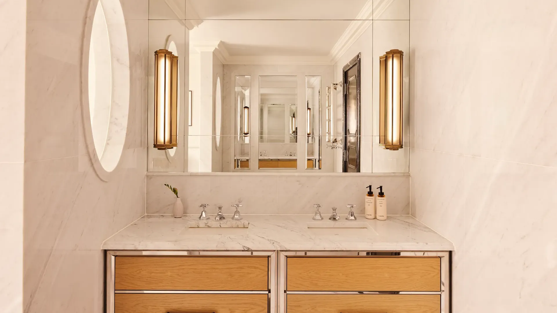 Marble bathroom vanity with double sinks, large mirror, wooden drawers, and wall lights.
