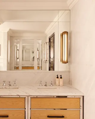 Marble bathroom vanity with double sinks, large mirror, wooden drawers, and wall lights.