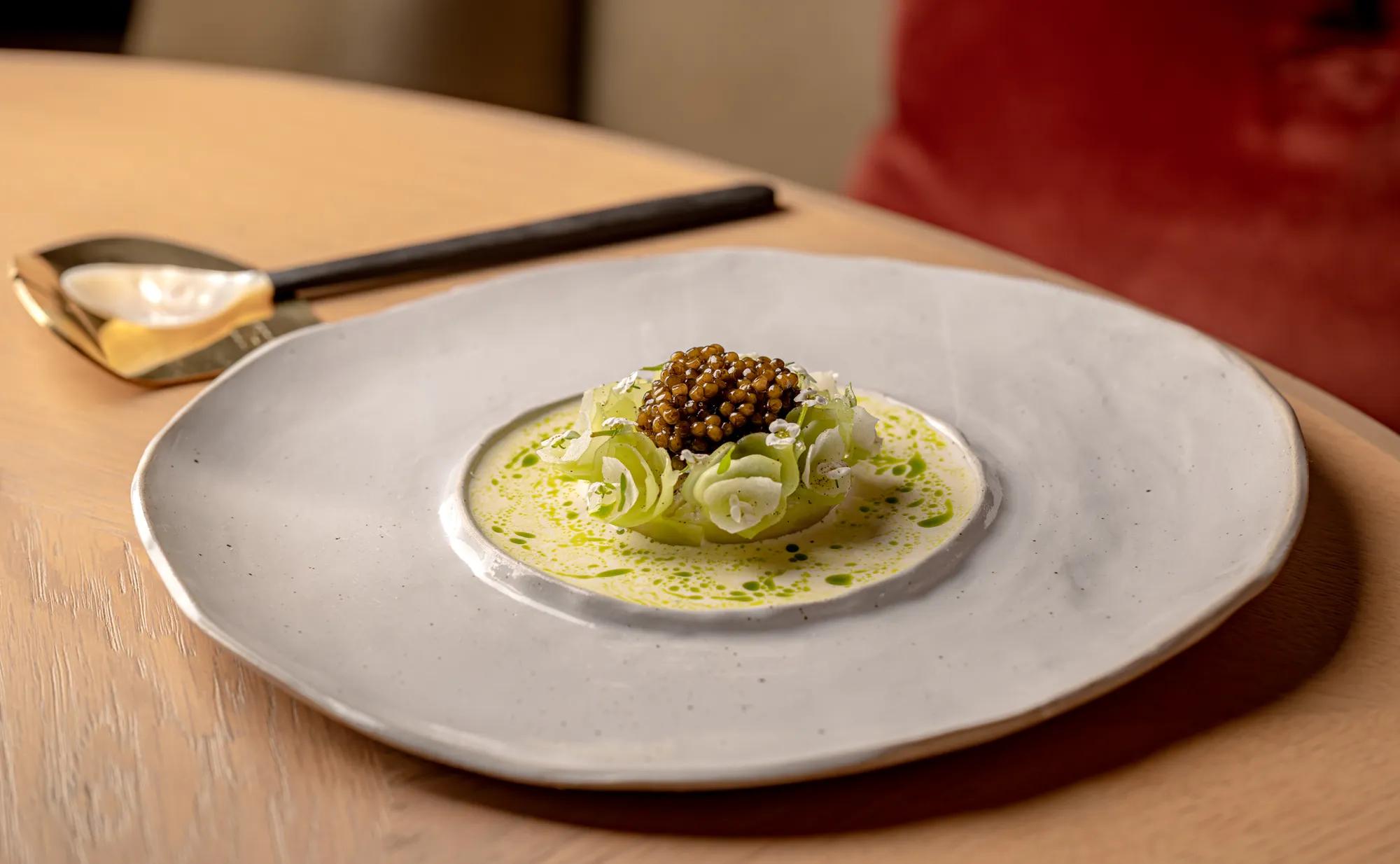 Plated dish with caviar atop ribboned vegetables in a light sauce, served in a shallow ceramic bowl