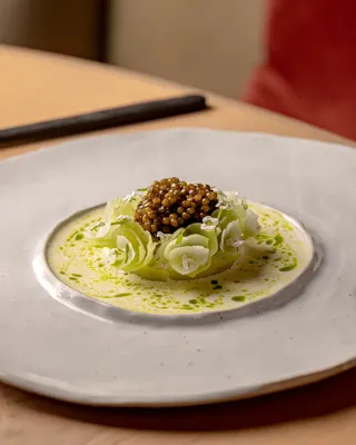 Plated dish with caviar atop ribboned vegetables in a light sauce, served in a shallow ceramic bowl