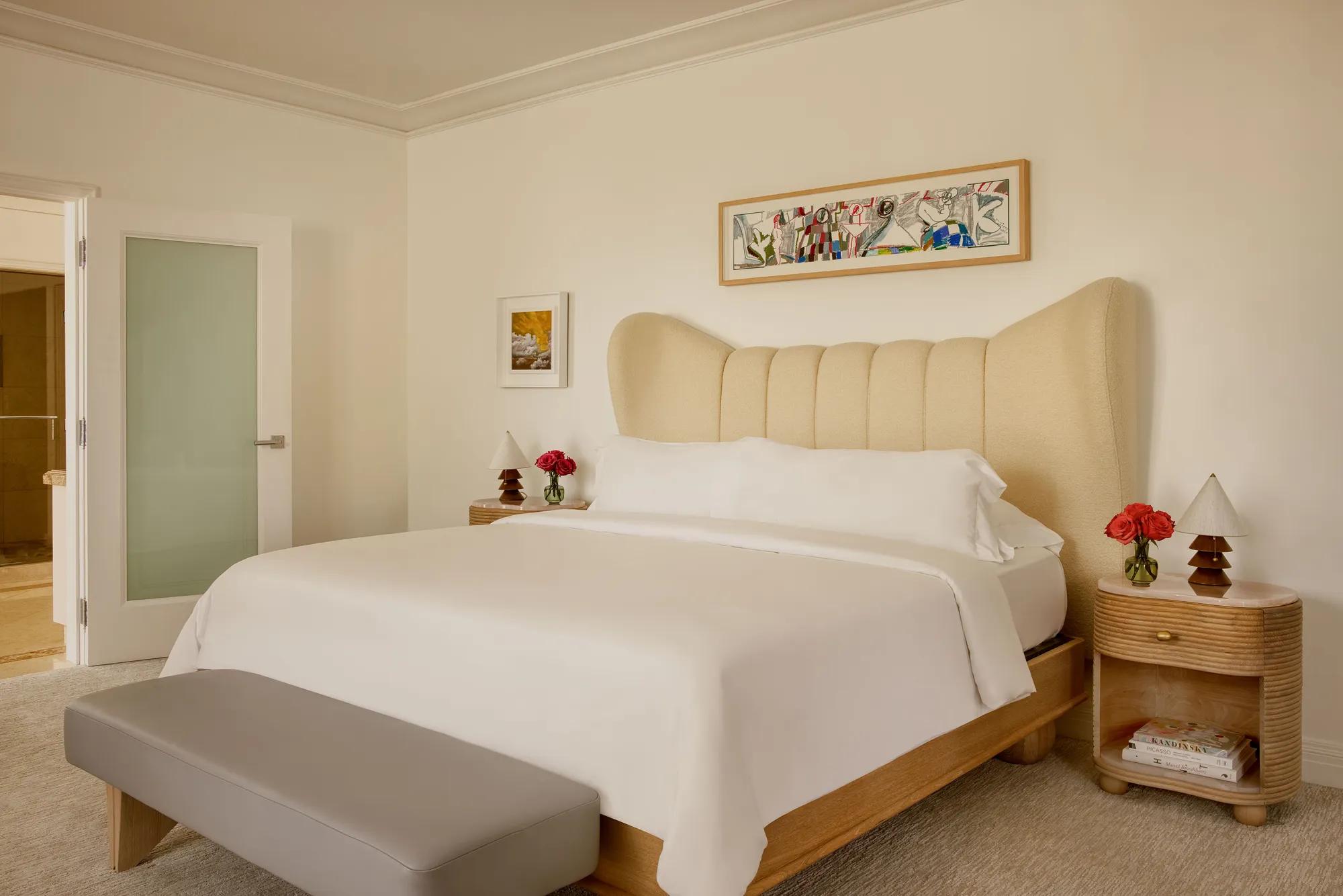 Hollywood Suite bedroom with king bed, soft linens, a large colorful artwork above the bed, and two wooden nightstands with fresh flowers.