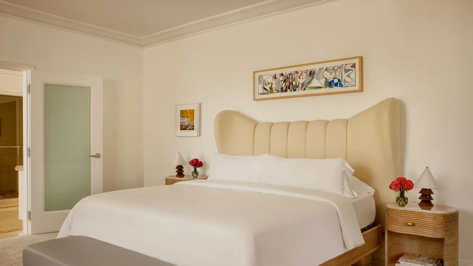 Hollywood Suite bedroom with king bed, soft linens, a large colorful artwork above the bed, and two wooden nightstands with fresh flowers.