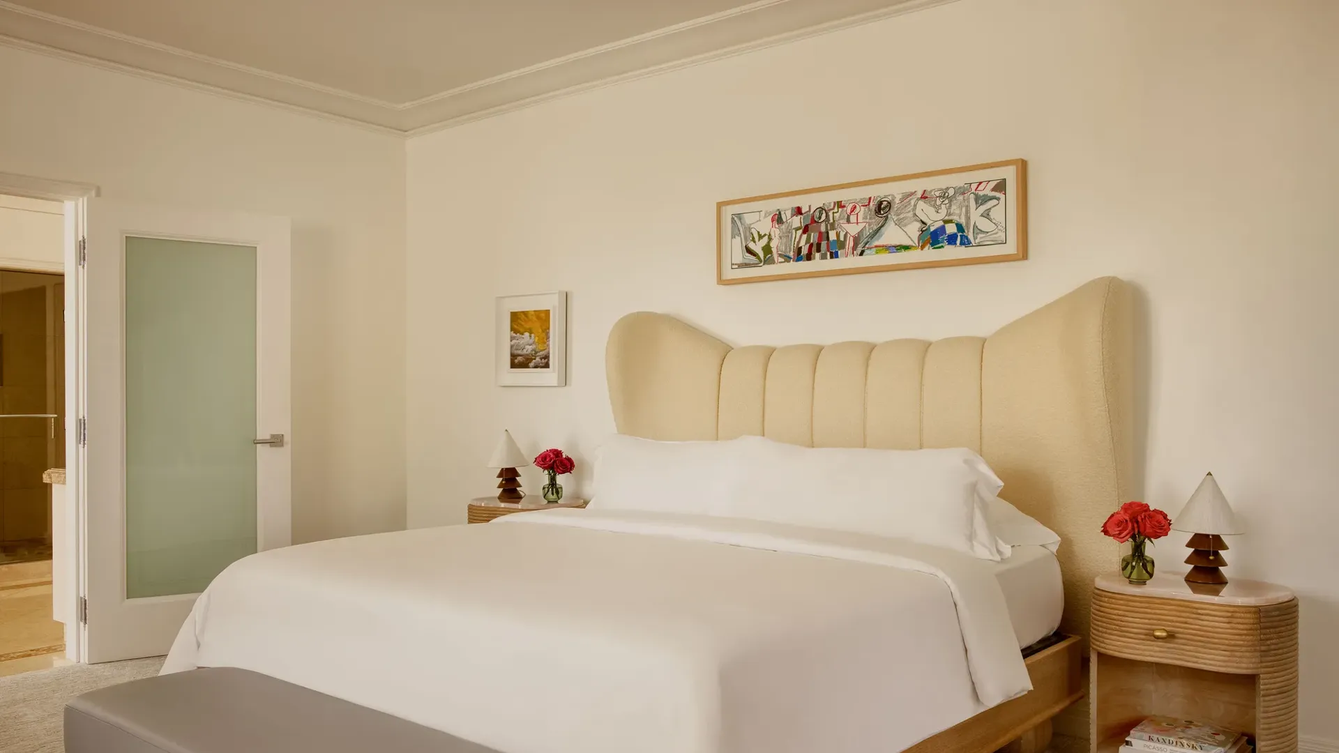 Hollywood Suite bedroom with king bed, soft linens, a large colorful artwork above the bed, and two wooden nightstands with fresh flowers.