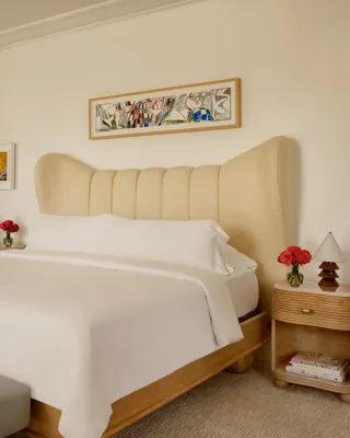Hollywood Suite bedroom with king bed, soft linens, a large colorful artwork above the bed, and two wooden nightstands with fresh flowers.