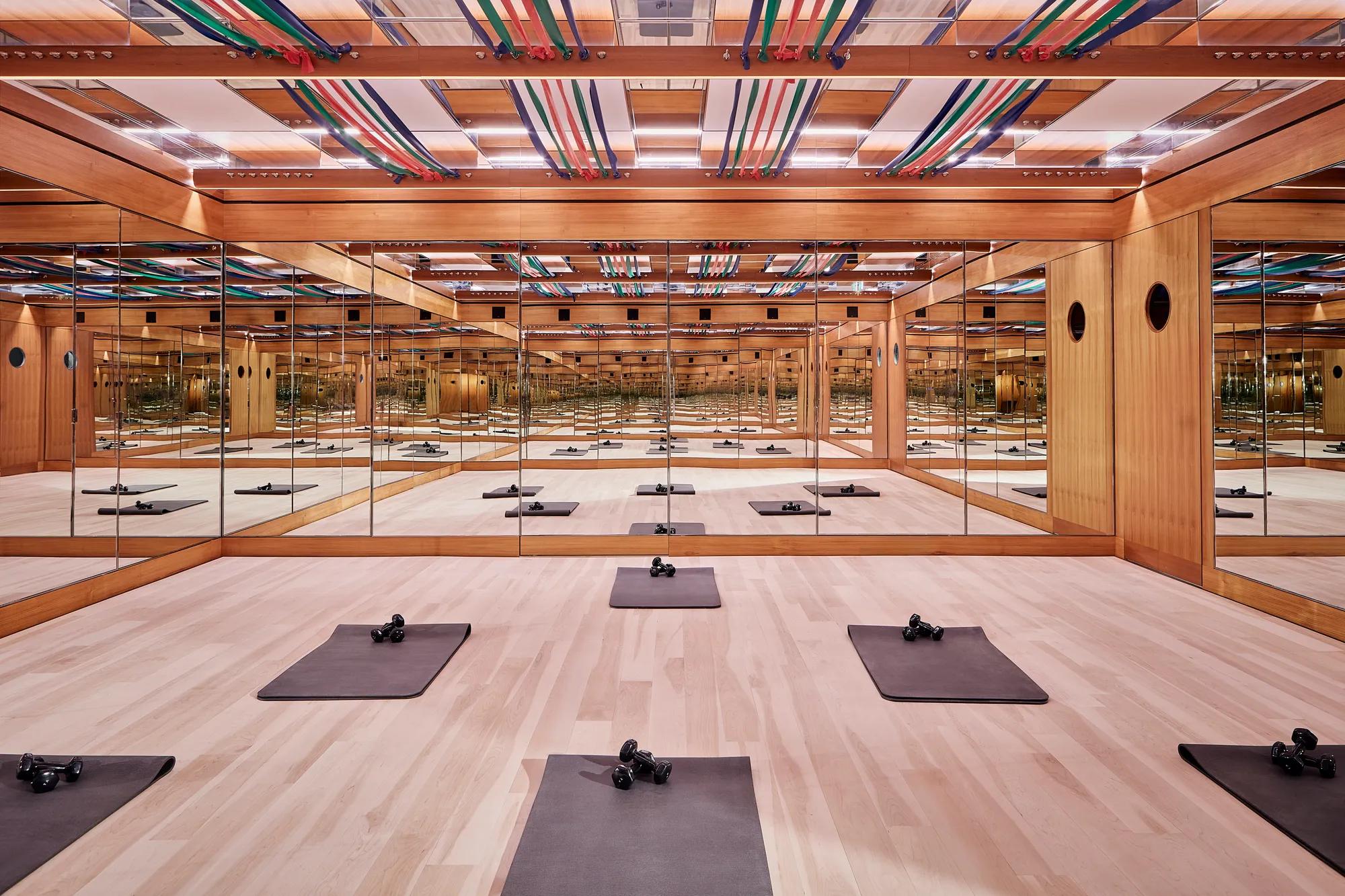 Mirrored fitness studio with wooden floors, exercise mats, dumbbells, and colourful ceiling straps, creating a calm, structured workout space.