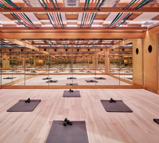 Mirrored fitness studio with wooden floors, exercise mats, dumbbells, and colourful ceiling straps, creating a calm, structured workout space.