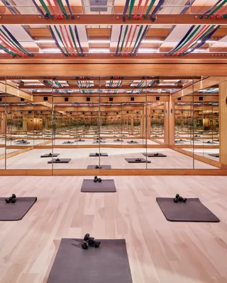 Mirrored fitness studio with wooden floors, exercise mats, dumbbells, and colourful ceiling straps, creating a calm, structured workout space.