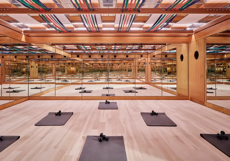 Mirrored fitness studio with wooden floors, exercise mats, dumbbells, and colourful ceiling straps, creating a calm, structured workout space.