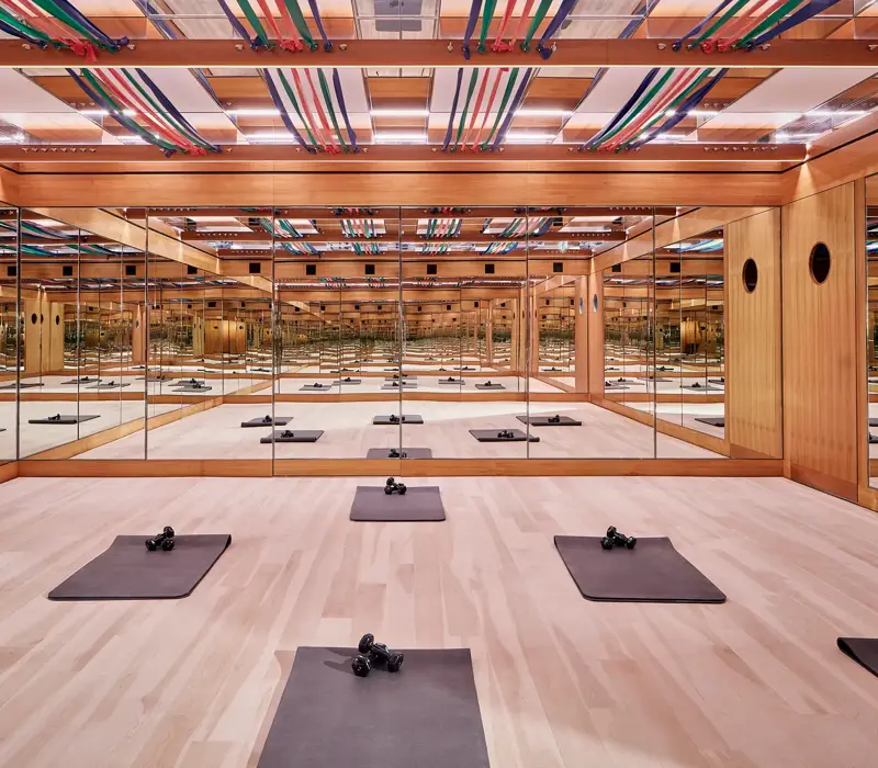 Mirrored fitness studio with wooden floors, exercise mats, dumbbells, and colourful ceiling straps, creating a calm, structured workout space.