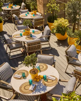 Rooftop terrace dining area with striped chairs, round tables, potted plants and views over surrounding city rooftops.