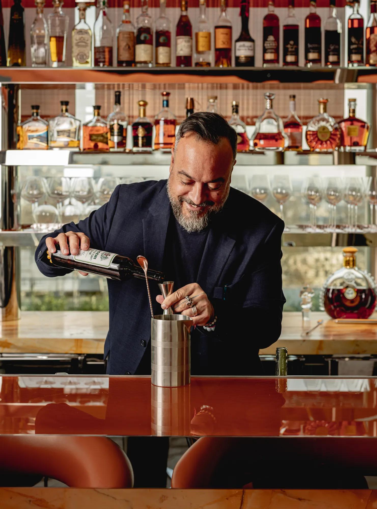 Bartender pours a drink at a well-stocked bar lined with spirits and glasses.