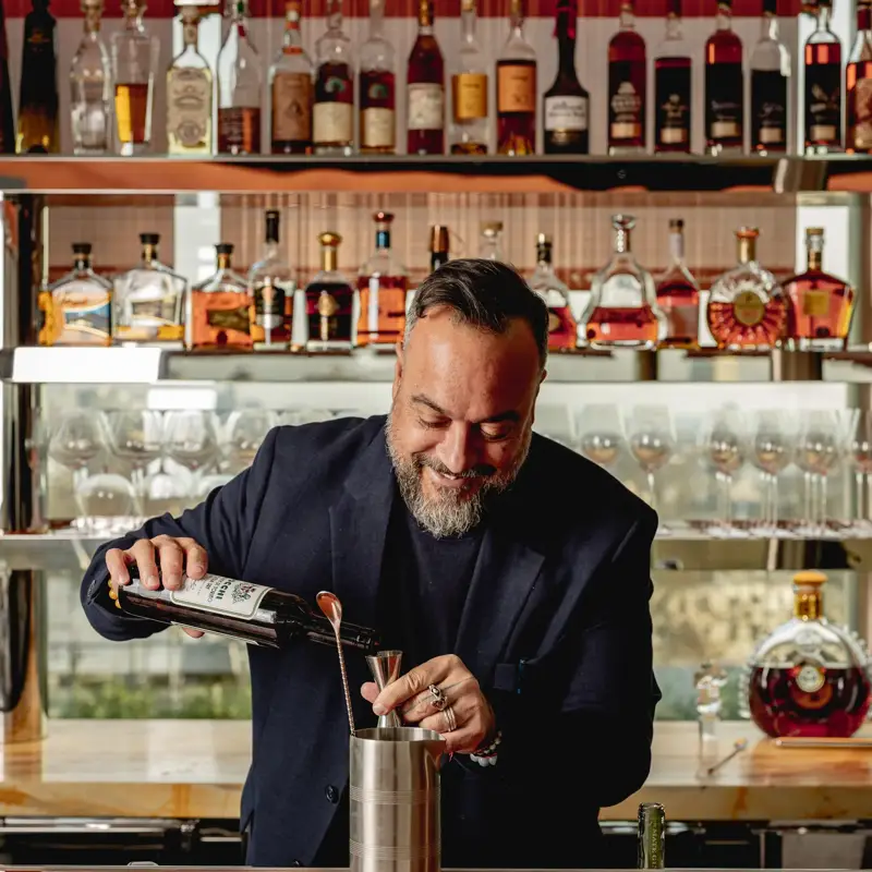 Bartender pours a drink at a well-stocked bar lined with spirits and glasses.