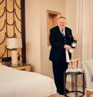 Butler standing in a well-appointed room, holding a bottle of champagne and dressed in formal uniform.