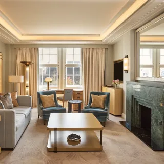 Contemporary living room with a sofa, two armchairs and a coffee table, centred around a green marble fireplace and framed by large windows.