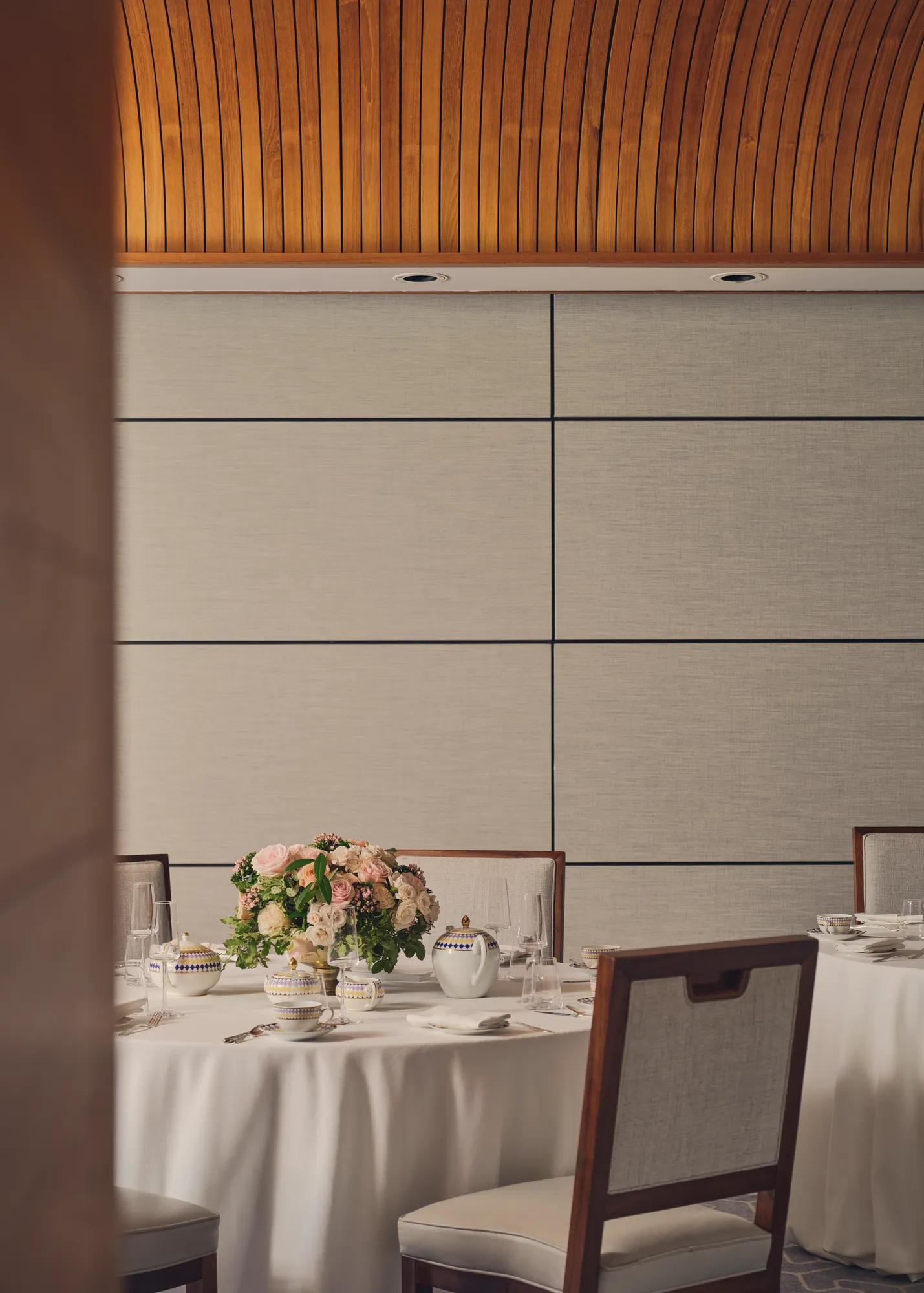 Elegant dining table with floral centerpiece set for afternoon tea under curved wooden ceiling.
