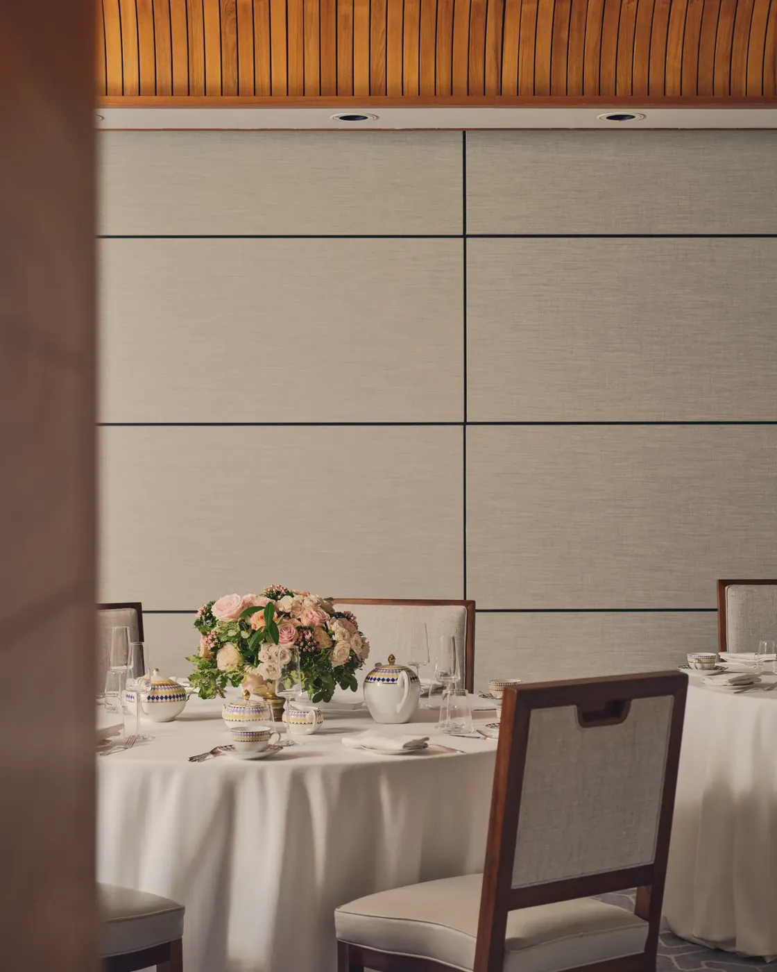 Elegant dining table with floral centerpiece set for afternoon tea under curved wooden ceiling.