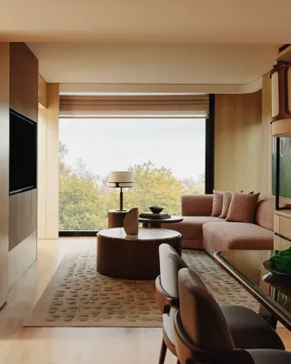 Spacious suite living and dining area with warm wood finishes, sofa seating, and large window overlooking trees.