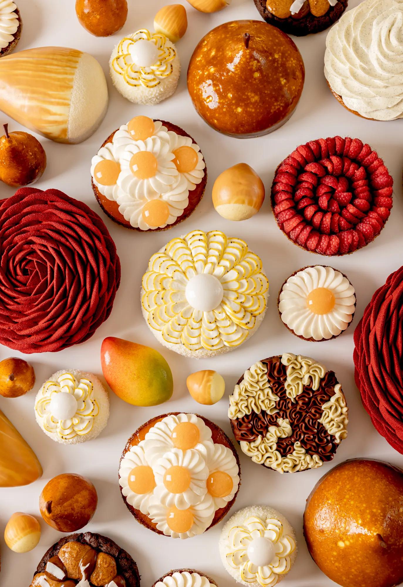 Assorted spring pastries with mango, grapefruit, pear and hazelnut, decorated with floral cream patterns, vibrant colors and glossy finishes