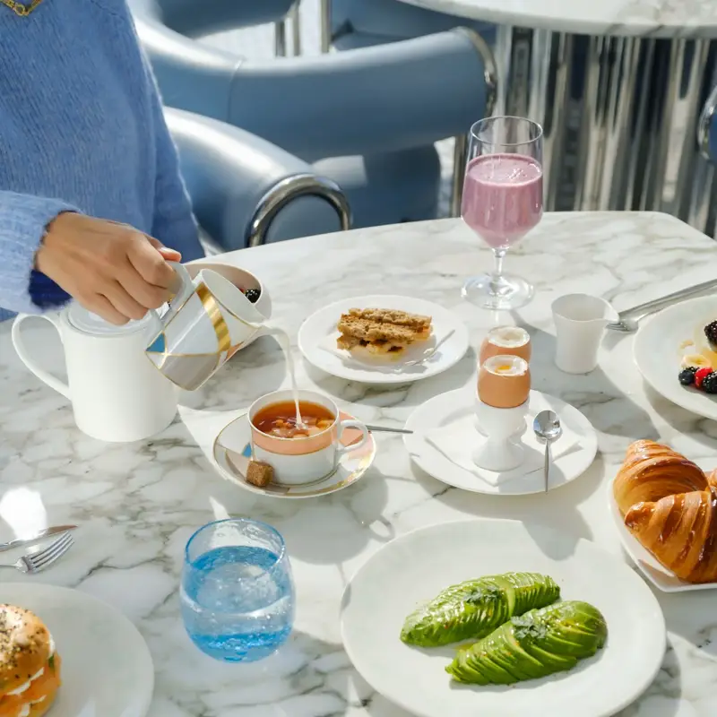 Petit-déjeuner élégant sur table en marbre, avec avocat, pâtisseries, granola, œuf à la coque et main versant du thé.