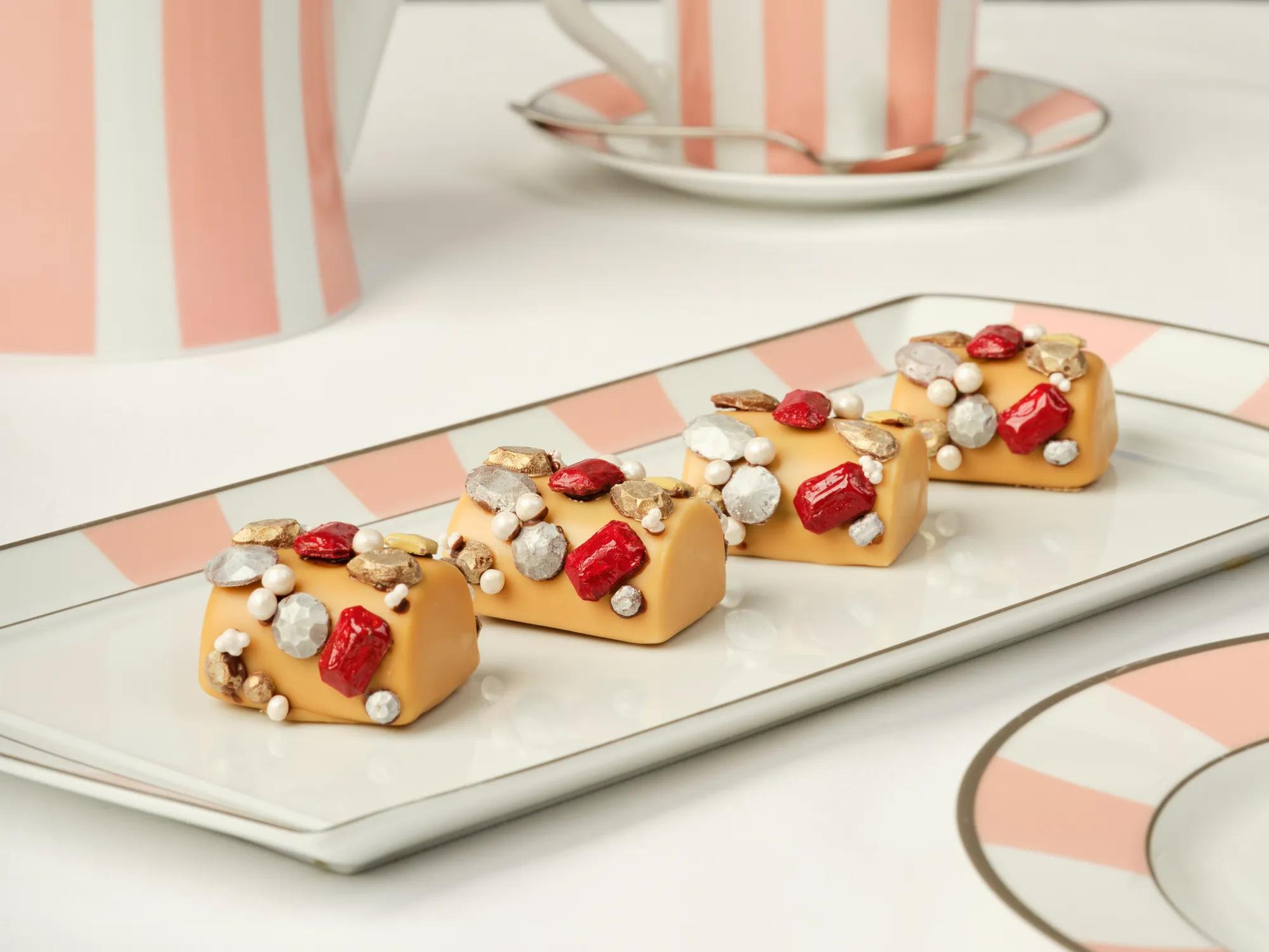 Caramel‑colored pastries topped with red, gold, and silver edible decorations on a striped tray.