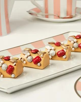 Caramel‑colored pastries topped with red, gold, and silver edible decorations on a striped tray.